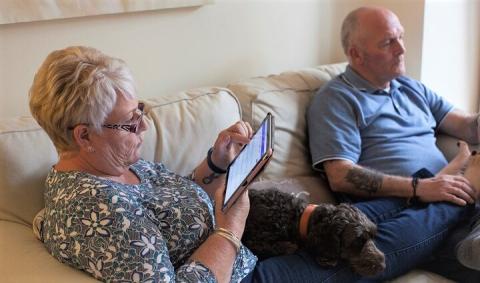 Two people sitting on a sofa, one of them is using an iPad